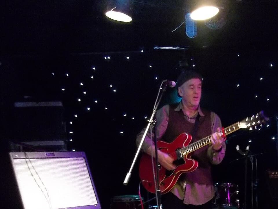 A musician performing with a guitar and microphone at an open mic night