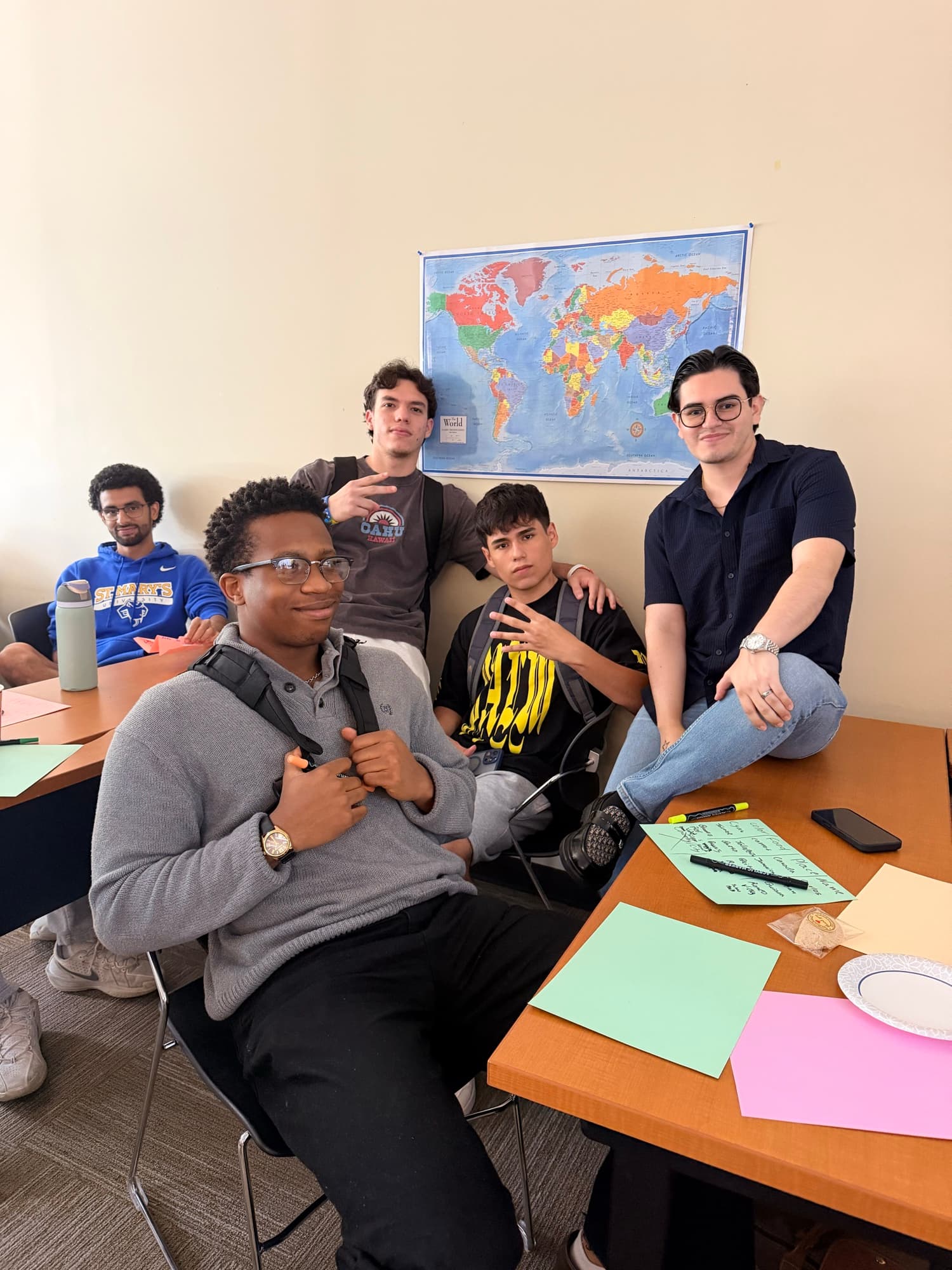 A group of We Glue students posing together in front of a world map