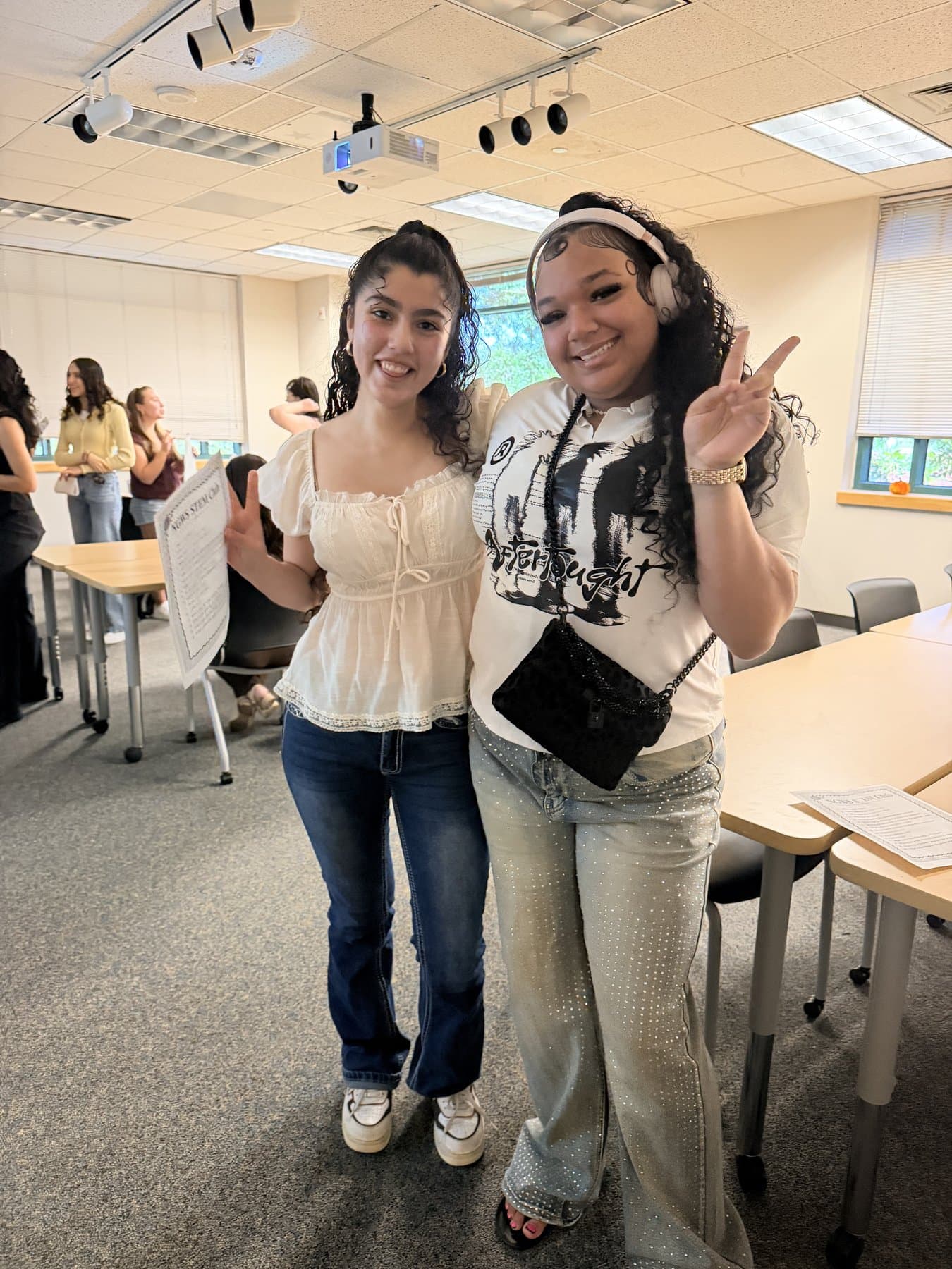 Two We Glue students throwing up peace signs in a classroom